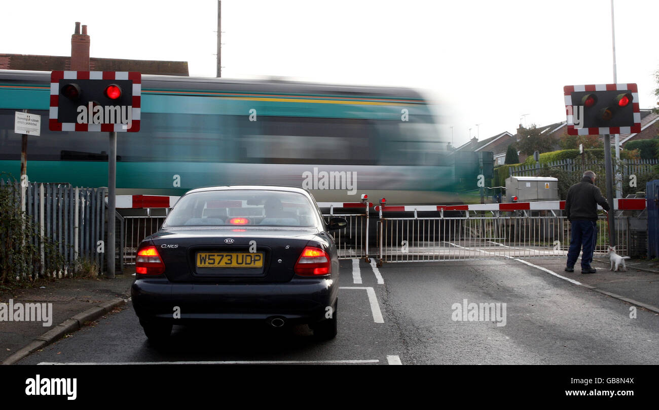 Une voiture et un piéton attendent à un passage à niveau pendant qu'un trian passe à Prestbury, Cheltenham, Gloucestershire. Banque D'Images