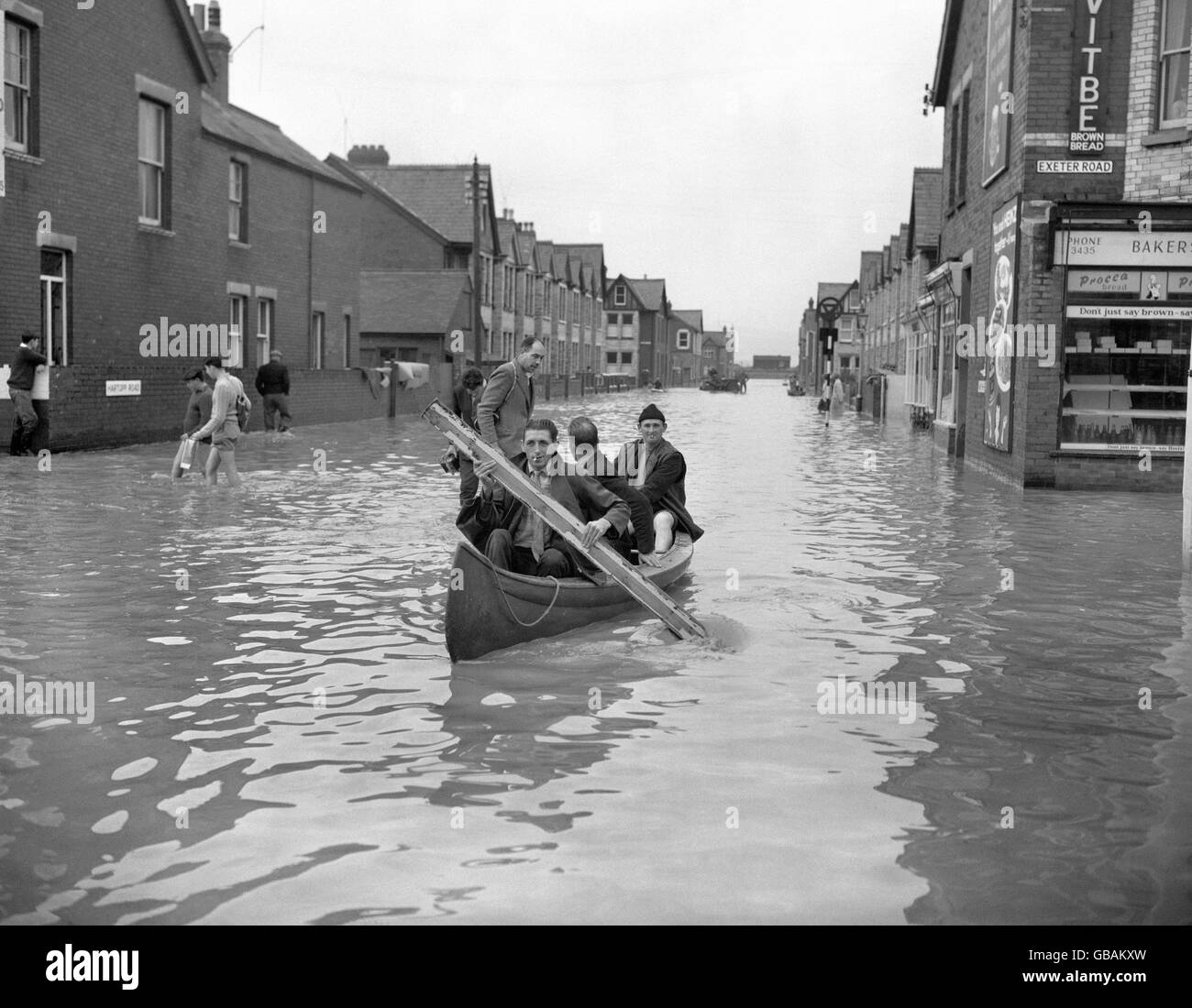 Un canoë pagayé d'un gros morceau de bois transporte trois hommes le long d'une rue transformée en canal 'vénitien' à Exmouth, le pire touché par les inondations désastreuses de Devon. Banque D'Images