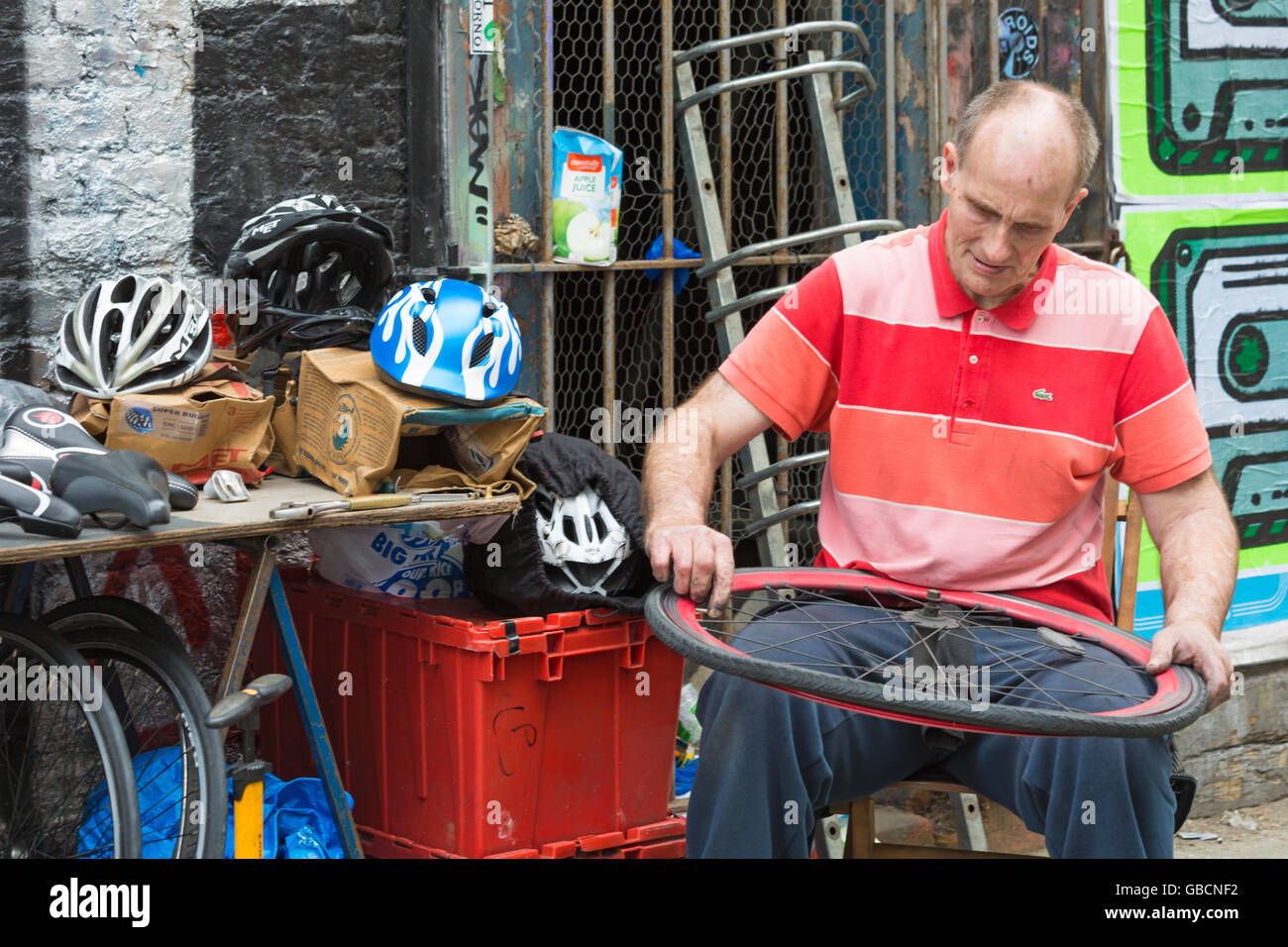 Le détenteur de la stalle de marché homme réparant la roue de vélo sur le marché par Brick Lane Shoreditch zone, Londres Royaume-Uni en juillet Banque D'Images