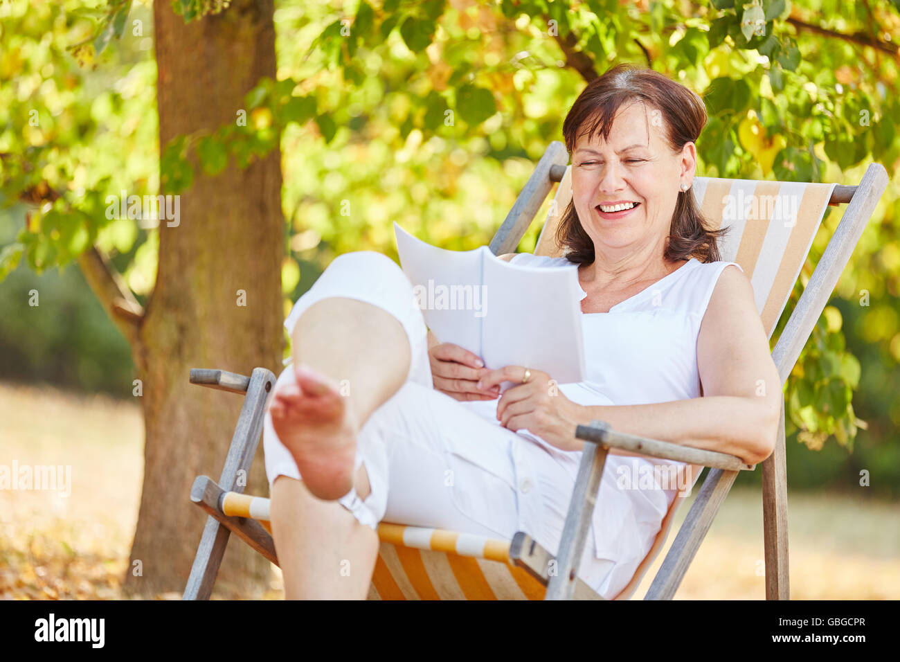 Senior woman reading détendue sur une chaise de terrasse en été dans le gardent Banque D'Images