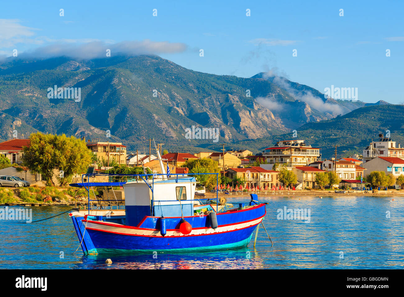 Bateau de pêche grec sur mer avec ses maisons colorées en arrière-plan à l'heure du lever sur l'île de Samos, Grèce Banque D'Images