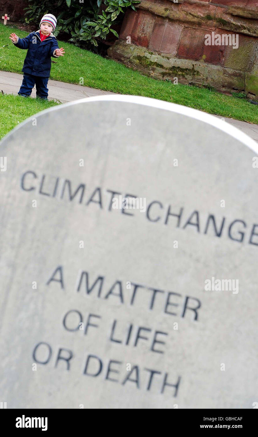 Un enfant se tient près d'une fausse tombe avec « changement climatique, UNE question de vie ou de mort » gravée sur elle, à l'extérieur de la cathédrale de Coventry. La tombe a été placée là pour mettre en évidence l'effet négatif du changement climatique sur les personnes vivant dans les pays en développement. Banque D'Images