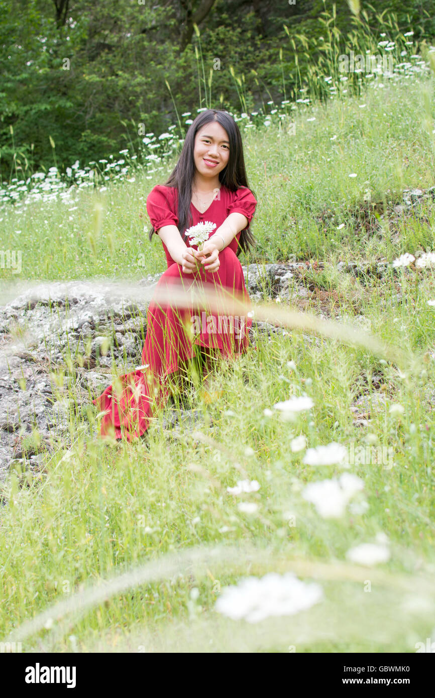 Jeune femme en robe rouge porte champ de fleurs Banque D'Images