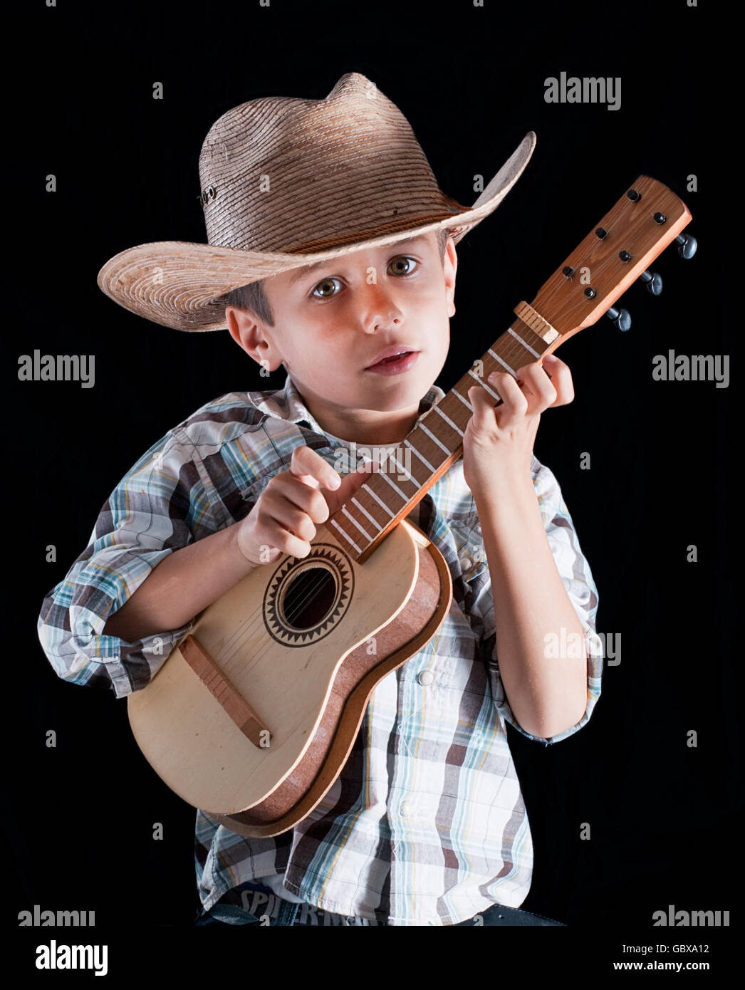 Un garçon portant un chapeau avec une guitare sur un fond noir Banque D'Images