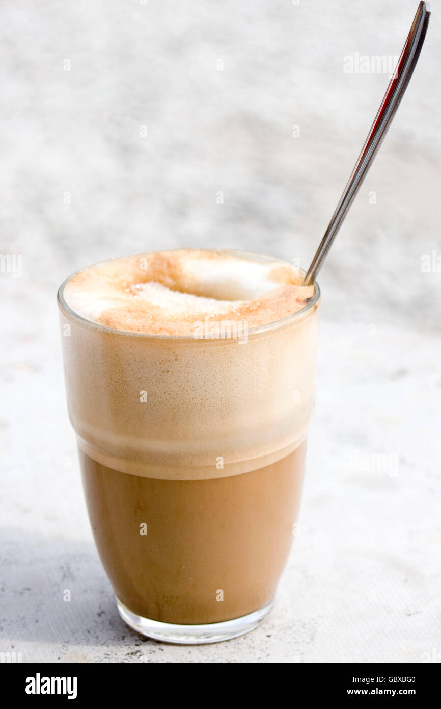 Un verre de caffè latte avec du sucre sur le dessus et une cuillère qui sort, assis sur une table de marbre Banque D'Images