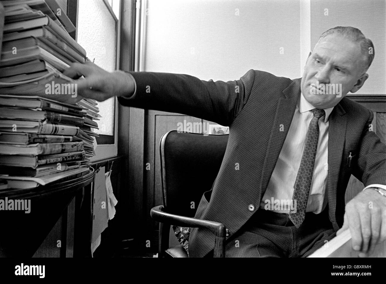 Bill Nicholson, directeur de Tottenham Hotspur, essaie de supprimer un livre de sa bibliothèque de bureau sans renverser la pile Banque D'Images