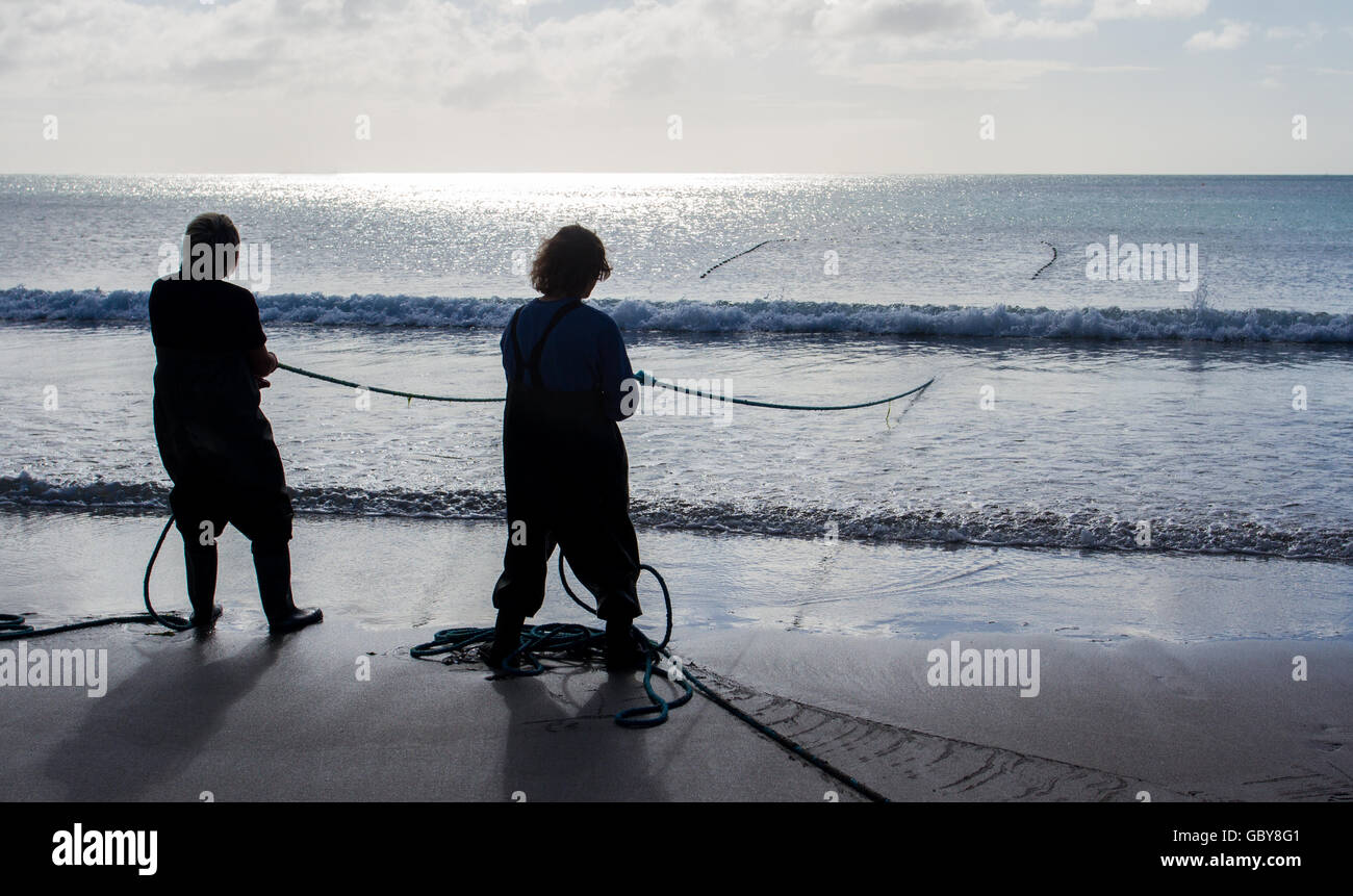 Les silhouettes de deux pêcheurs cornouaillais debout sur une plage au lever et transporter leurs filets dans les poissons qu'ils aux lançons. Banque D'Images
