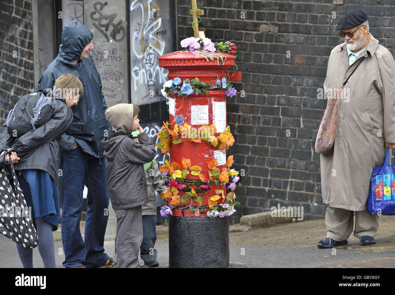 Les gens regardent une boîte postale à Bedminster, Bristol, qui a été transformée en une œuvre d'art, ornée de poésie, de fleurs et d'insignes religieux, après qu'elle a été retirée de l'usage public. Banque D'Images