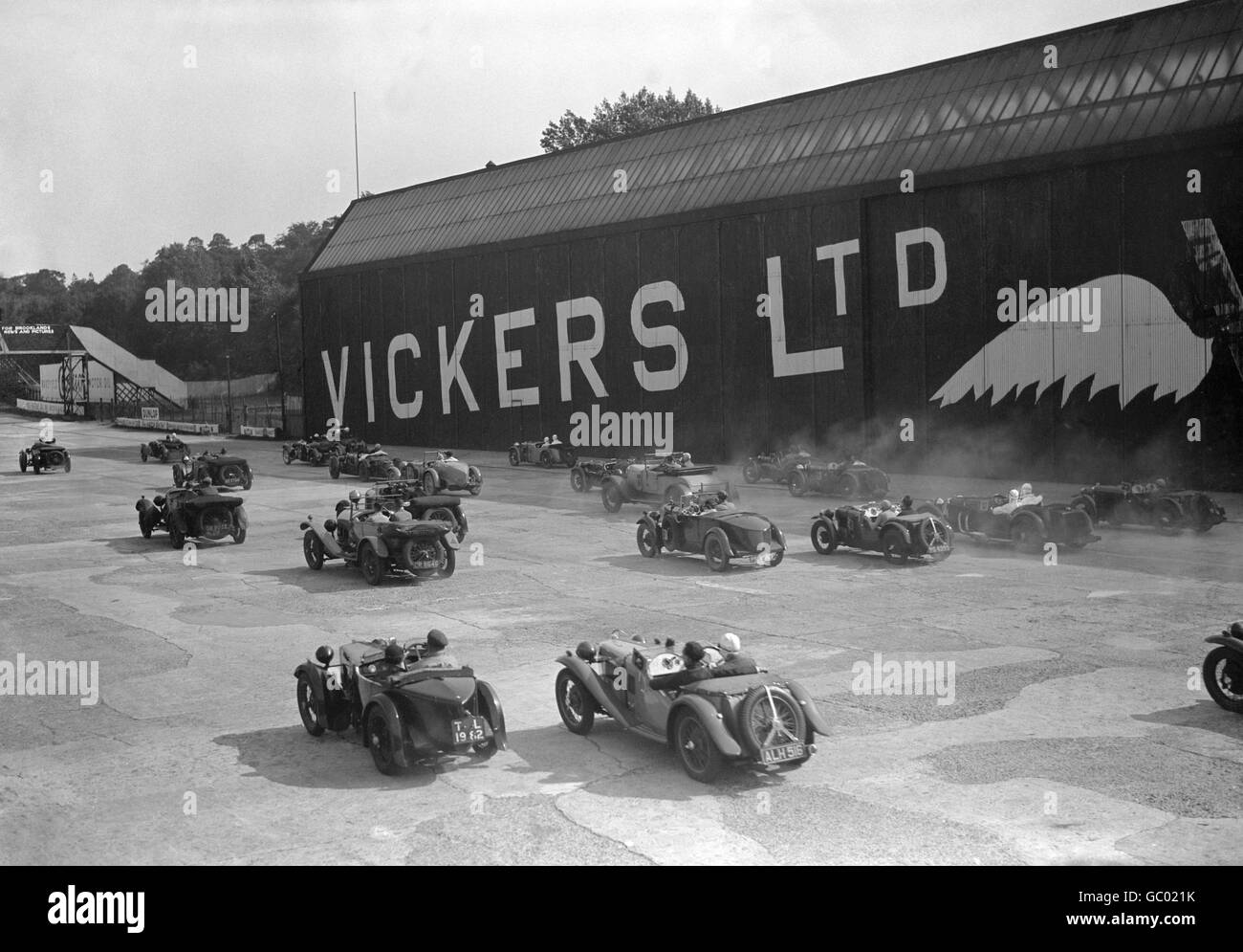 Des voitures passant devant les abris Vickers à la fourche sur le circuit de course de Brooklands. Banque D'Images