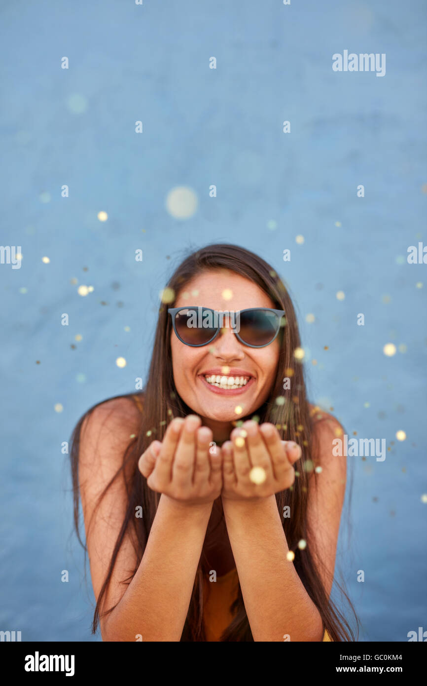 Shot of young woman blowing sparkles sur fond bleu. Caucasian female model blowing confetti dans l'air et smili Banque D'Images