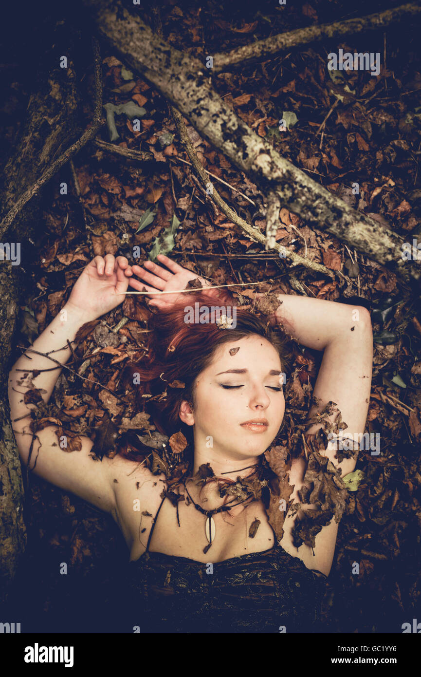 Beauté de sommeil : Une jeune femme rousse aux cheveux rouge fille seule dans une forêt allongée sur le dos sur les feuilles, les yeux fermés, les bras au-dessus de sa tête, endormi, rêvant Banque D'Images