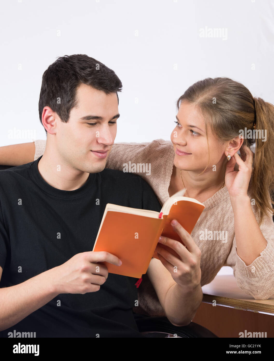 Young casual couple reading livre orange, homme porte noir T-shirt noir, est assis sur une chaise, femme se tient derrière Banque D'Images