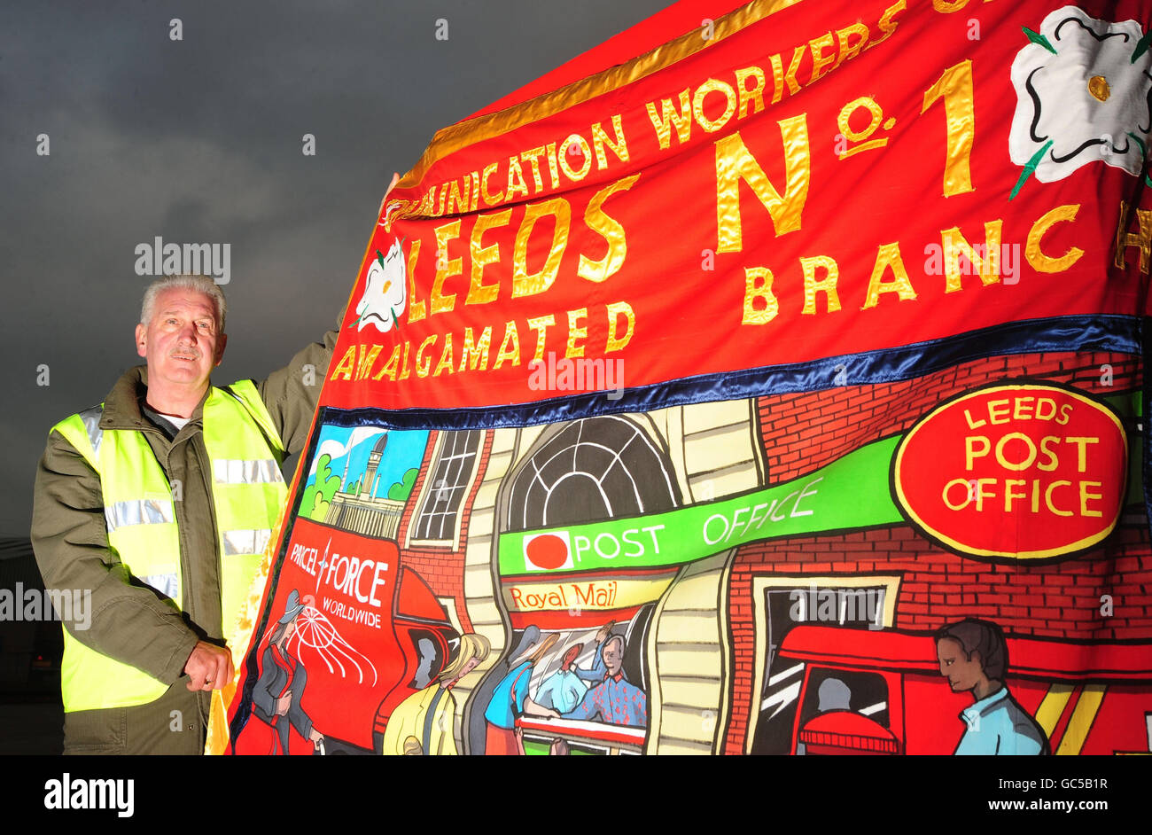 Danny McGougan, travailleur du Royal Mail, détient la bannière de sa succursale locale à l'extérieur du dépôt de Stourton Royal Mail à Leeds. Banque D'Images