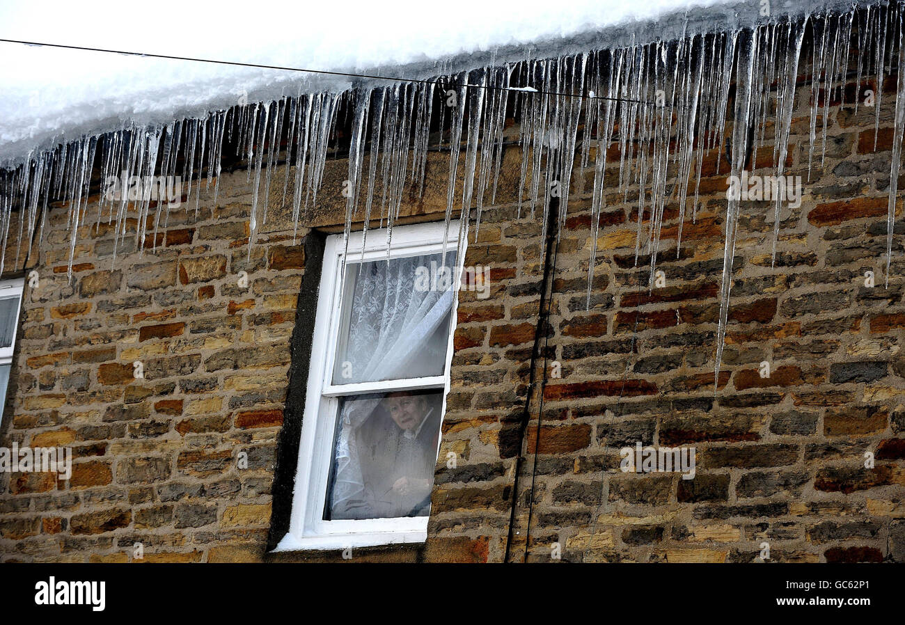 Une femme regarde par sa fenêtre à Allendale, dans le Northumberland, comme de grandes glaces pendent du toit après de fortes chutes de neige. Banque D'Images