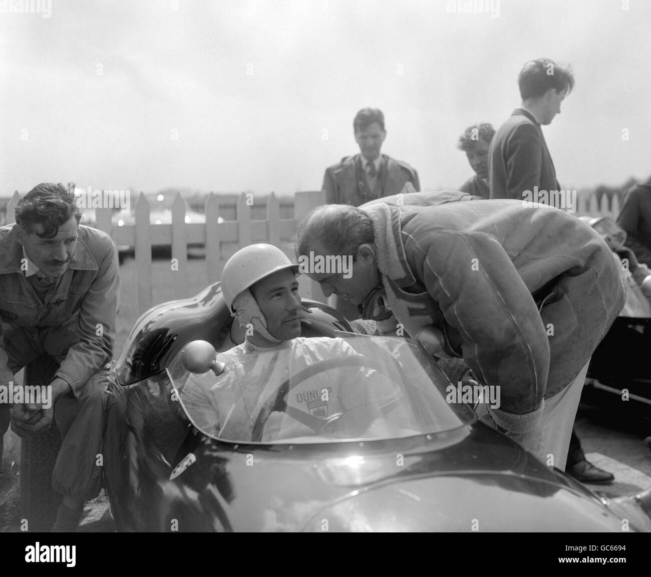 Stirling Moss, pilote de course britannique, assis dans une Porsche de l'équipe de course RRC Walker, parlant au pilote de course Harry Schell, avant de léter le circuit de Goodwood en préparation à l'événement automobile britannique du lundi de Pâques. Banque D'Images