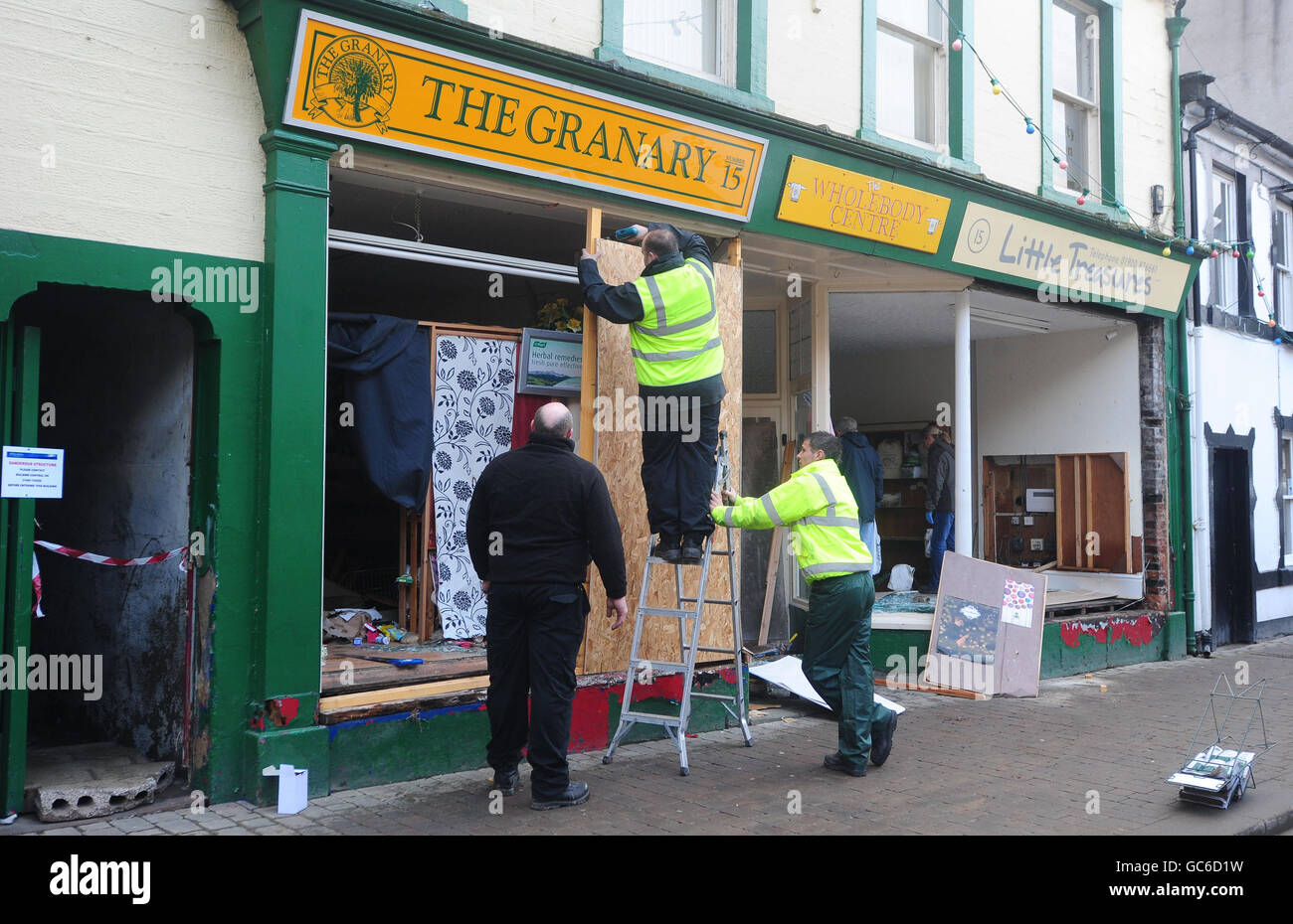 Les hommes de travail commencent à monter dans les boutiques de Cockermouth High Street après que les eaux d'inondation ont reculé. Banque D'Images