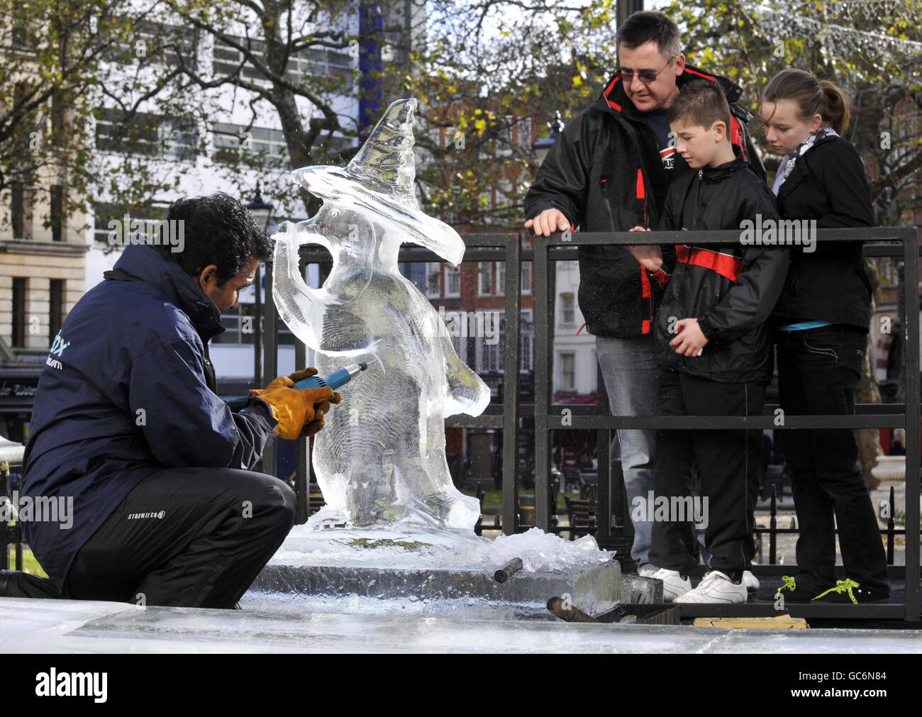 Les gens se tiennent sur une plate-forme derrière une sculpture sur glace d'un pingouin dans Leicester Square à Londres, qui a été créé pour promouvoir le début d'une campagne de Noël West End pour encourager les gens à magasiner et à manger dans la région. Banque D'Images