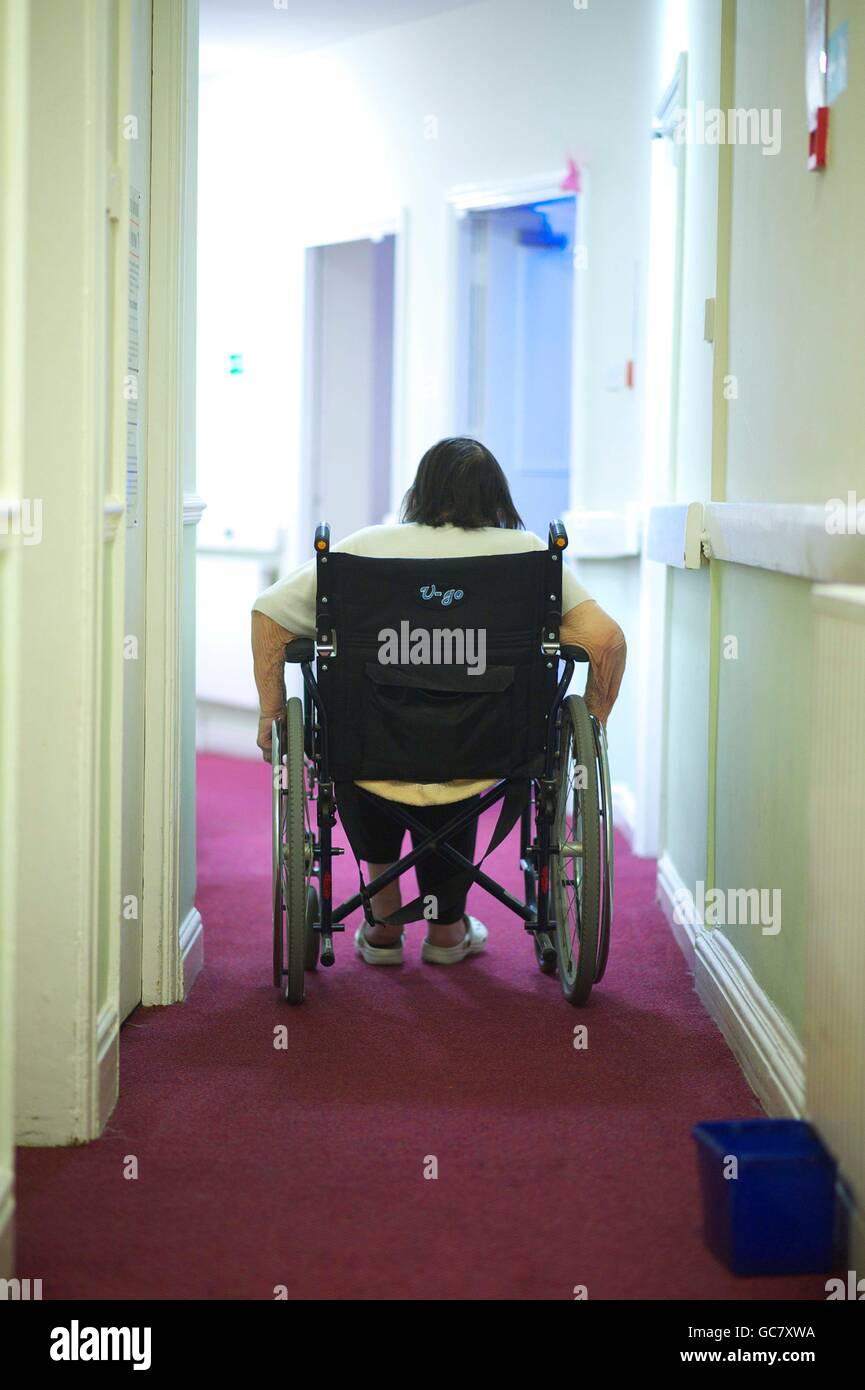 Des femmes âgées dans une maison de soins de patients souffrant de démence pousse elle-même dans un fauteuil roulant dans le couloir Banque D'Images