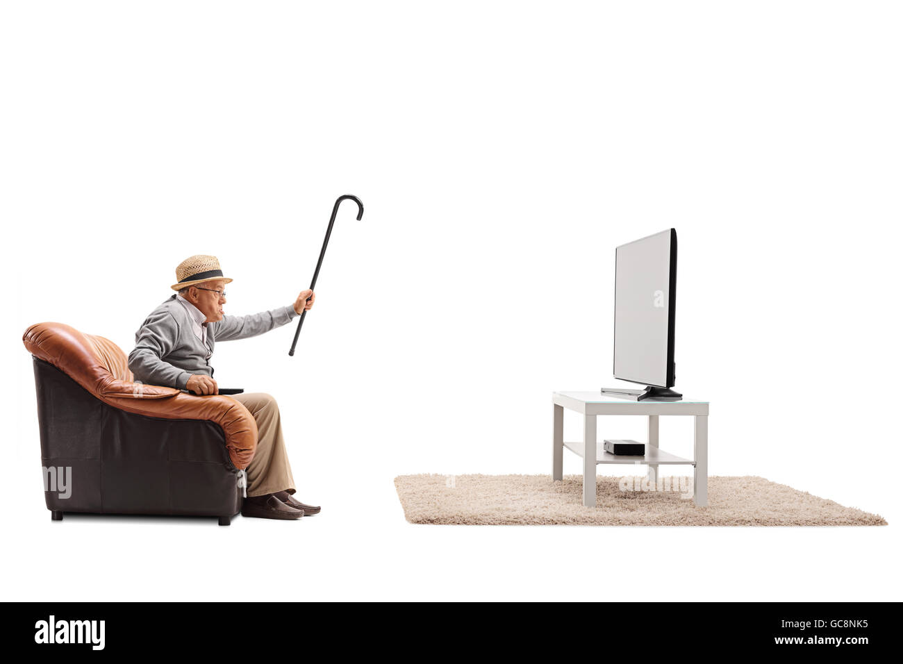 Senior en colère devant la télévision et menaçant avec sa canne vers le plat isolé sur fond blanc Banque D'Images