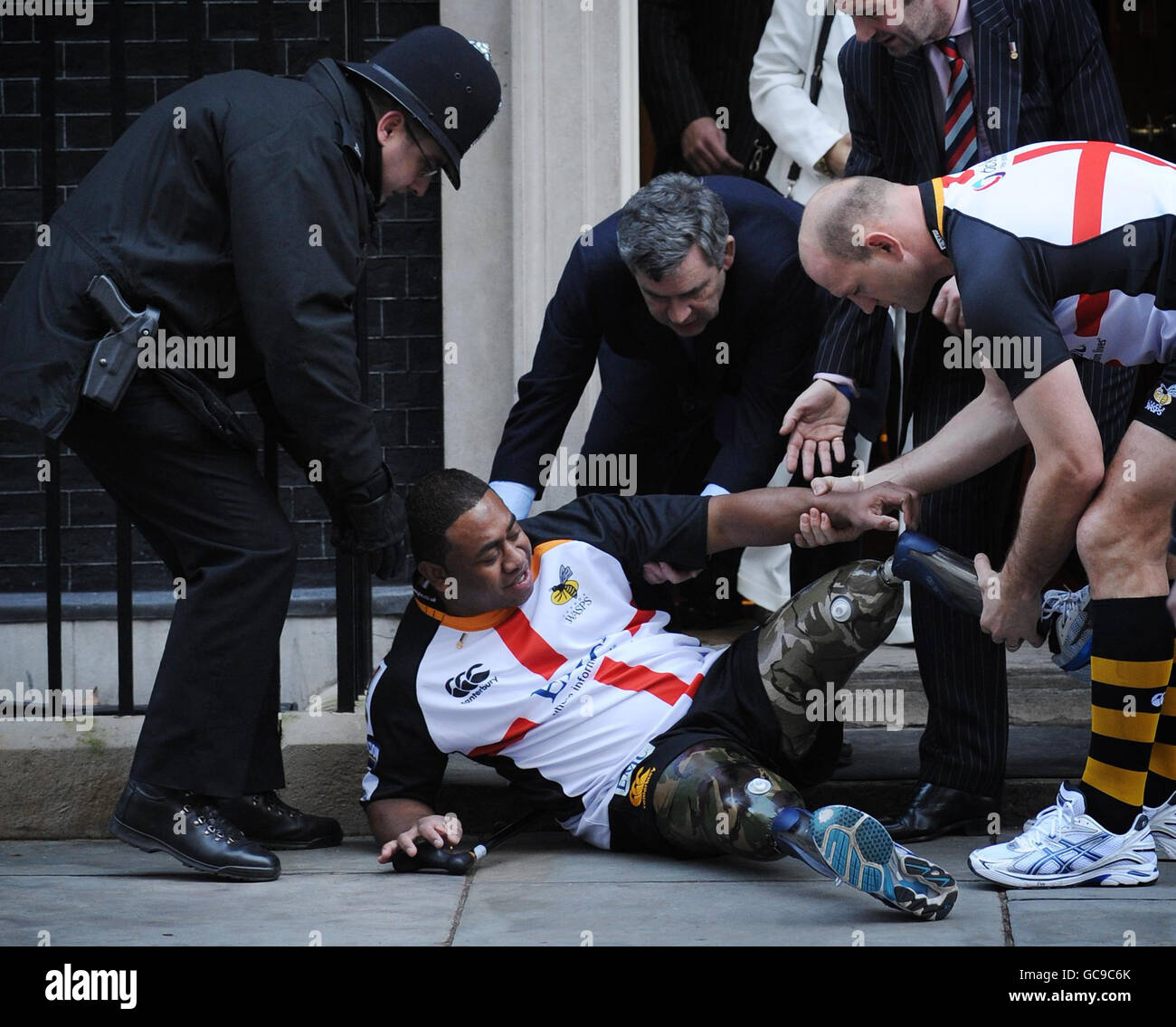 Le premier ministre Gordon Brown et le joueur de rugby Lawrence Dallaglio(à droite) aident le double amputé Derek Derenalagi après qu'il est tombé à la porte du 10 Downing Street, Londres. L'ancien soldat qui a perdu les deux jambes en Afghanistan en 2007 était là pour promouvoir un match de rugby du Saint-Georges Day afin de recueillir de l'argent pour aider les héros. Banque D'Images