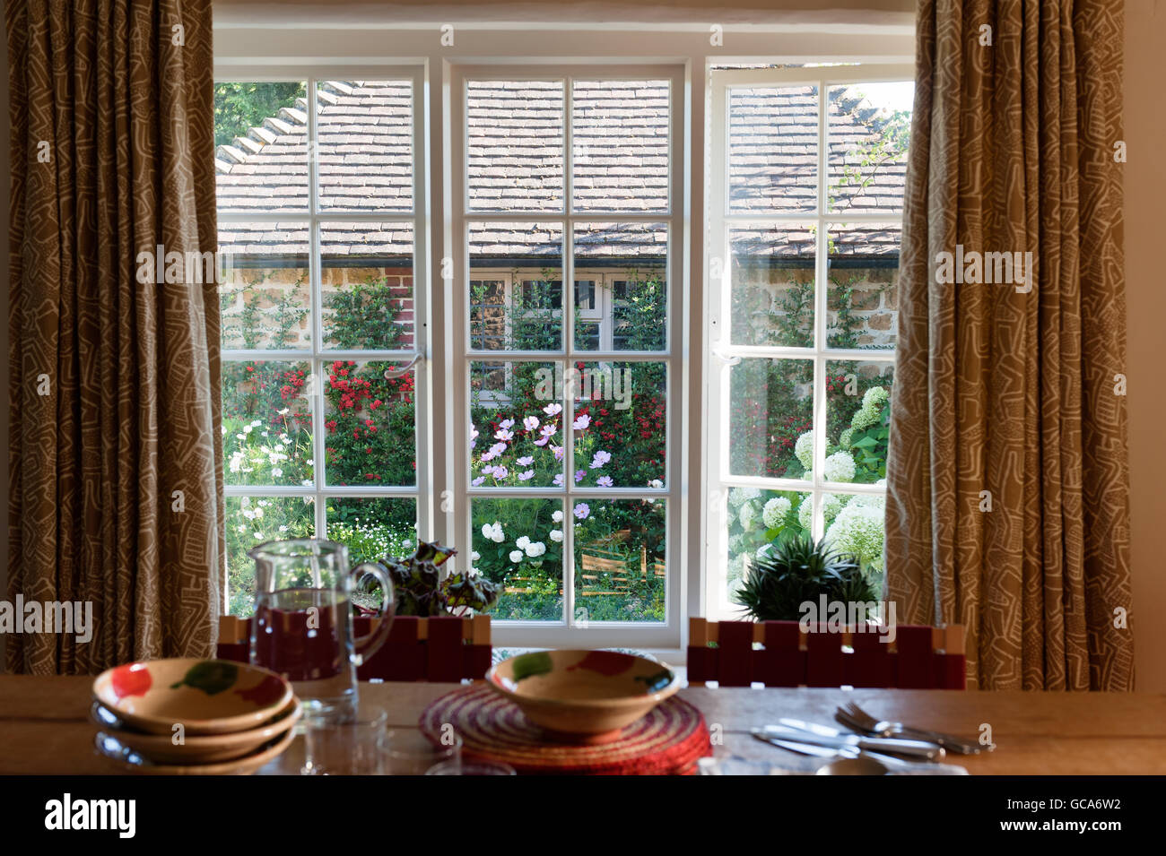 Vue à travers la fenêtre de la salle à manger Jardin en floraison. Le tissu des rideaux est Saibo par Raoul de textiles en provenance de George Smith. Banque D'Images
