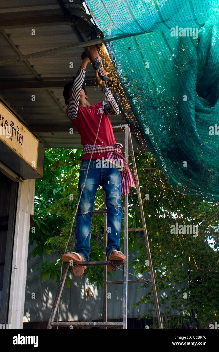 Un homme à l'aide d'une scie circulaire est l'outil de forage pouvoir créer des étincelles en métal sciage Chork, village au Cambodge. Banque D'Images