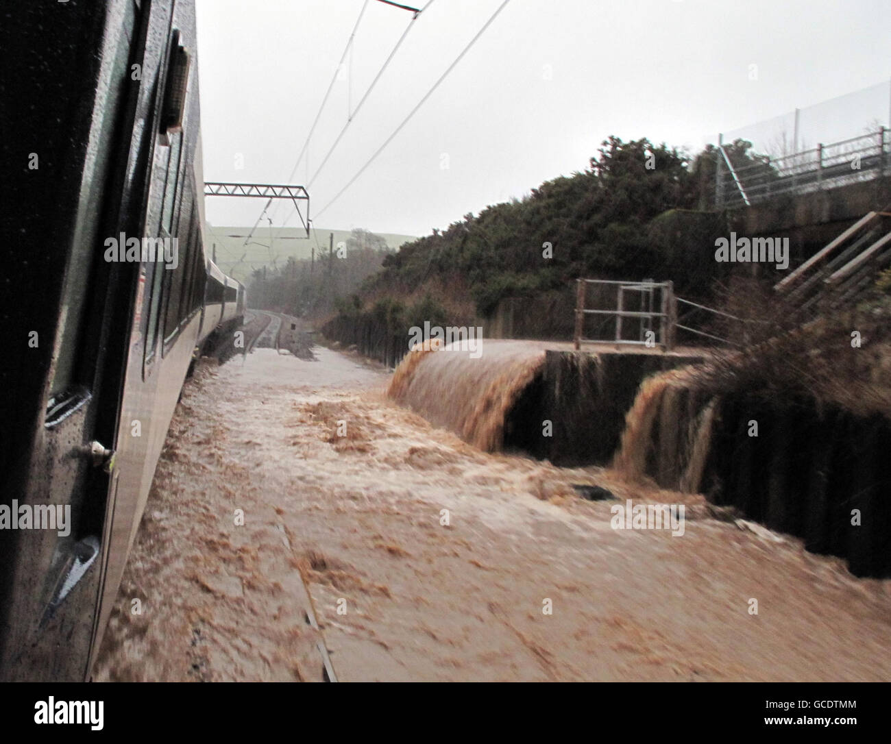 L'eau d'une rivière aux frontières qui a fait éclater ses inondations de rive sur la ligne principale de la côte est au nord de Berwick, entraînant un ralentissement des trains à un rythme de marche. Banque D'Images