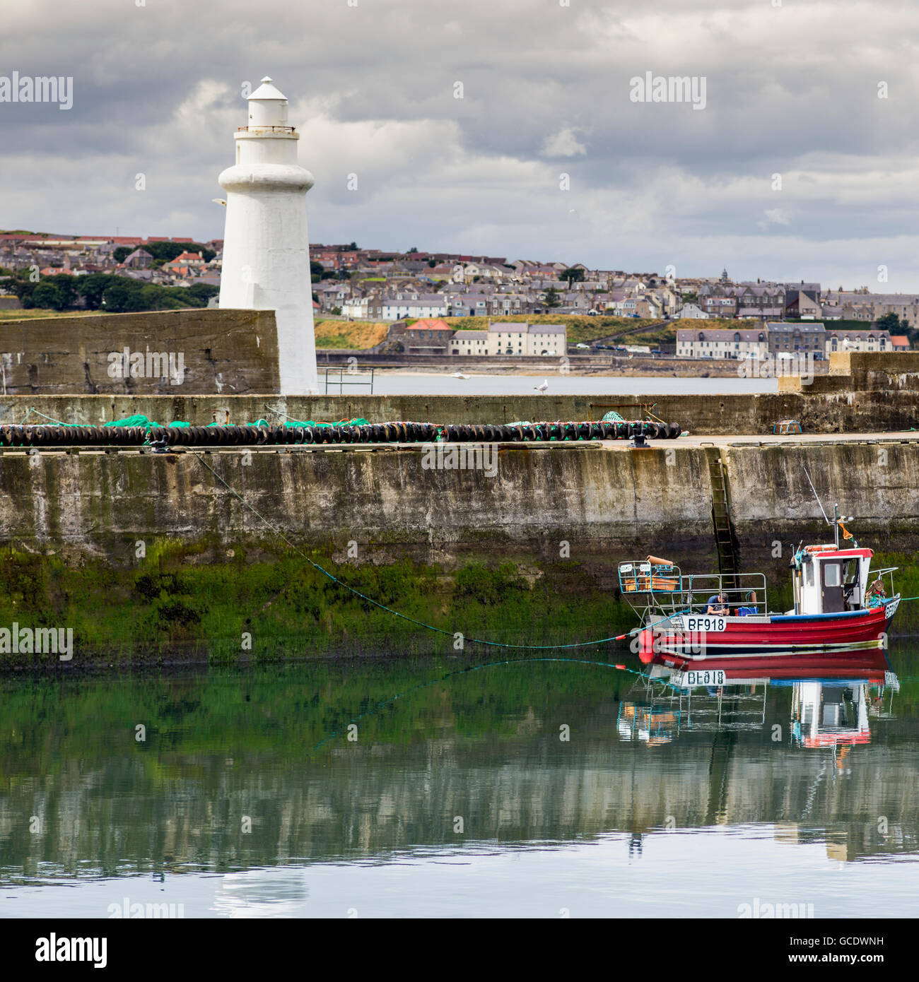 Bateau de pêche amarré dans un port tranquille avec un phare blanc et paysage urbain ; Macduff, Aberdeenshire, Scotland Banque D'Images