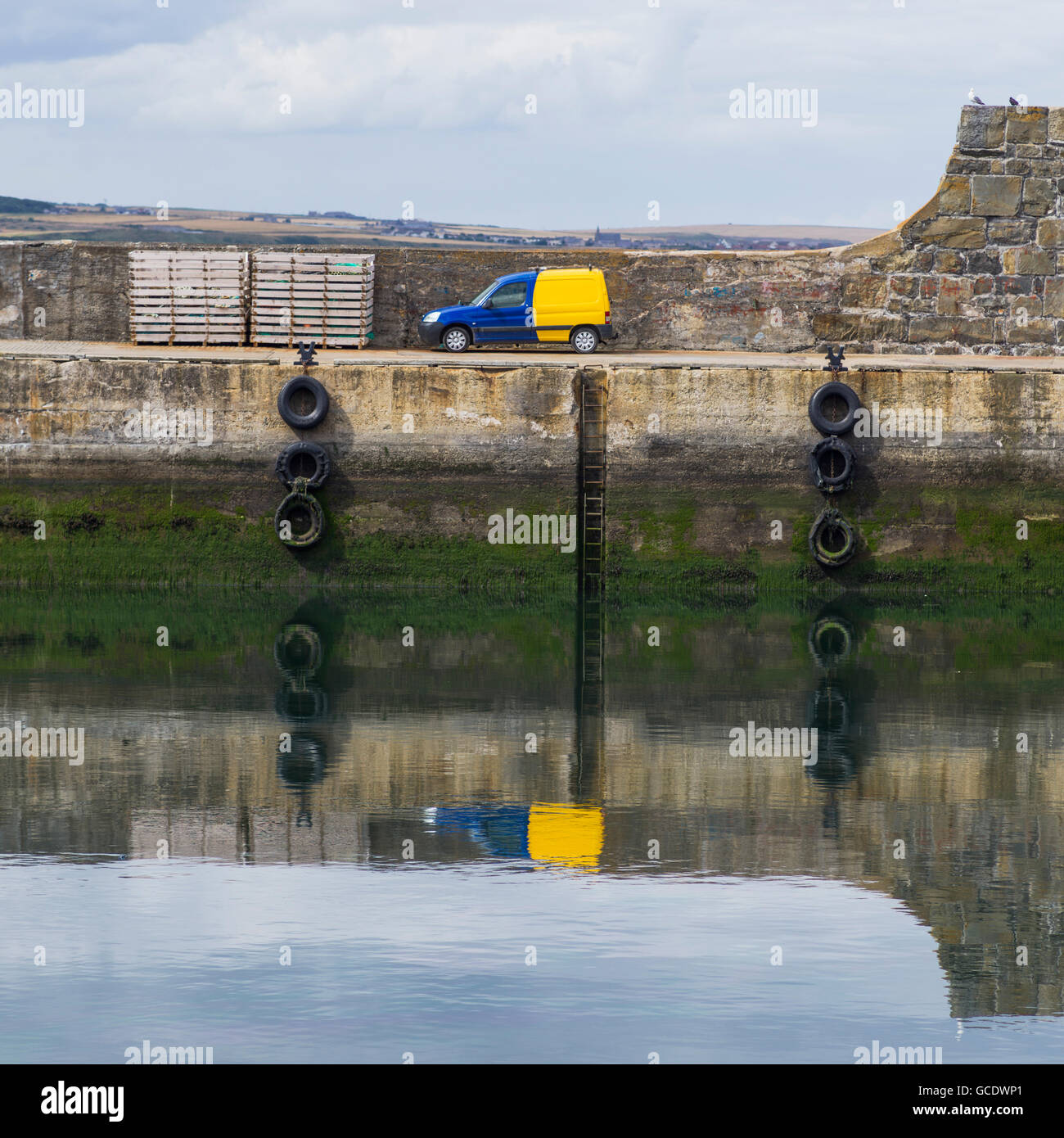 Un camion bleu et jaune garé au bord de l'eau et se reflètent dans le port ; Macduff, Aberdeenshire, Scotland Banque D'Images