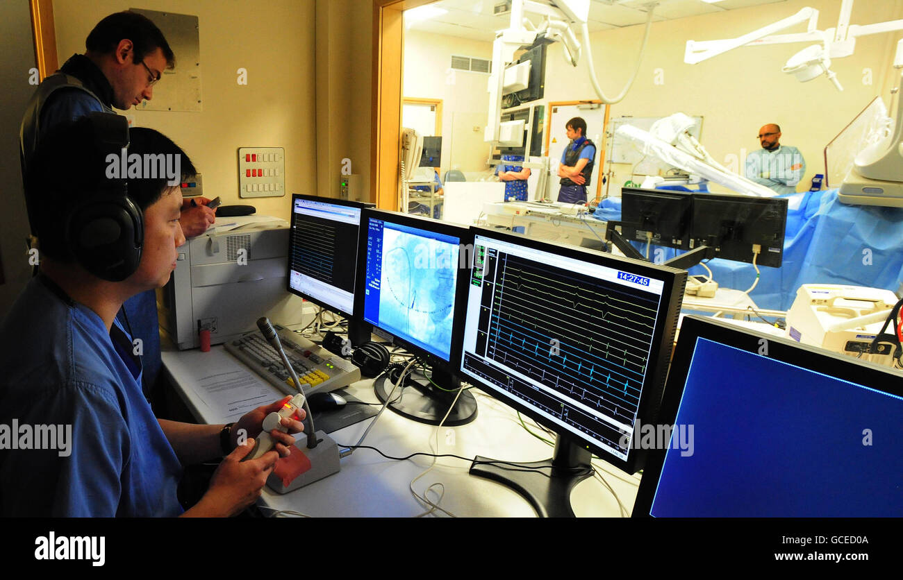 Le Dr Andre ng, chirurgien (première à gauche) cardiologue consultant à l'hôpital de Glenfield et maître de conférences en sciences cardiovasculaires à l'université de Leicester, regarde un écran pendant qu'il guide un cathéter à l'aide d'un bras robotisé à l'hôpital de Glenfield à Leicester, Au cours de la première opération cardiaque à distance au monde réalisée avec le bras sur le patient Kenneth Crocker, 70, de Burton on Trent. Banque D'Images