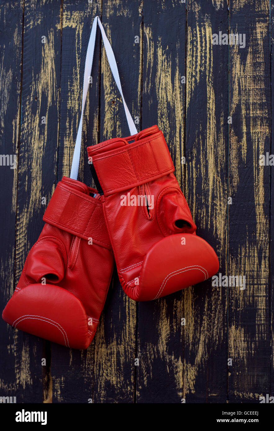 Gants de boxe rouge suspendu à un clou sur un mur en bois noir Banque D'Images