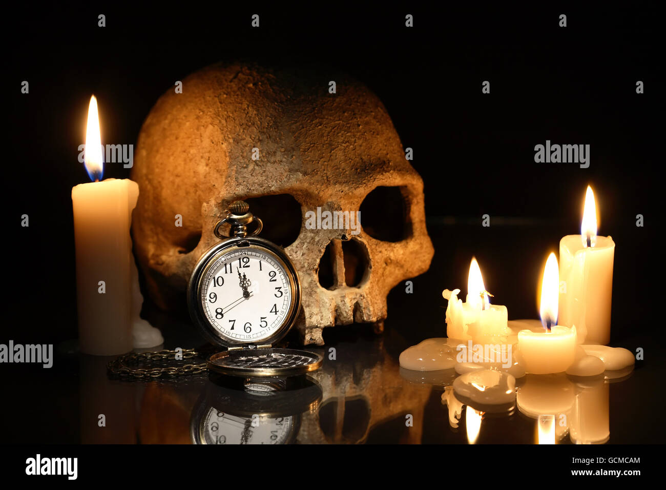 Concept de la mort. Un crâne humain et montre de poche près de bougies d'éclairage sur fond sombre Banque D'Images