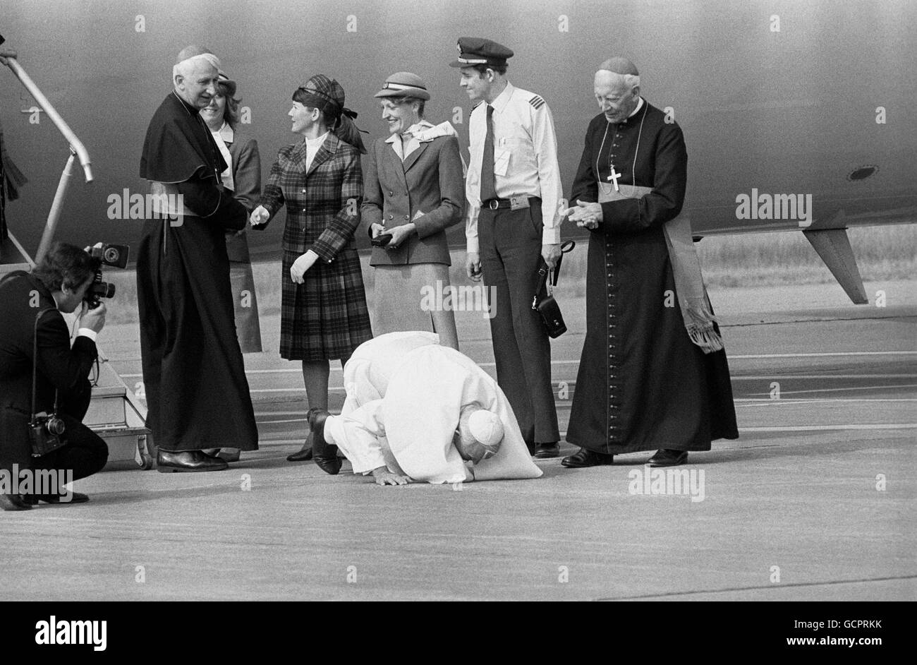 Le pape Jean-Paul II s'agenouille et embrasse le sol lorsqu'il arrive au pays de Galles le dernier jour de son voyage de six jours en Grande-Bretagne, accompagnant le Pape est l'archevêque de Westminster, le cardinal Basil Hume, vu serrer la main avec le personnel de l'aéroport. Banque D'Images
