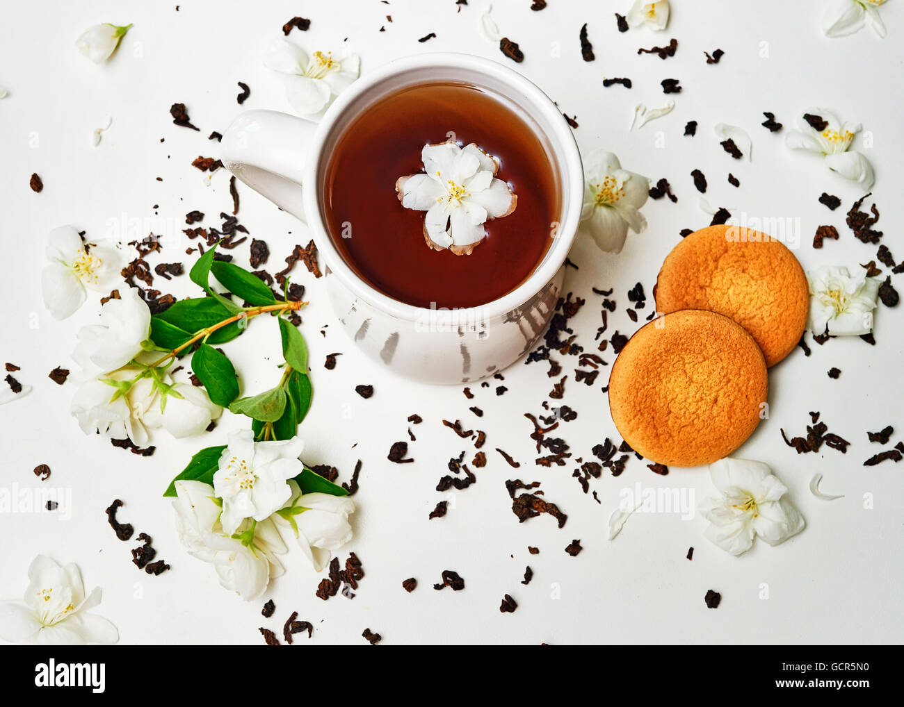 Tasse de thé avec des feuilles séchées et des fleurs fraîches de jasmin parfumé et biscuit sur fond blanc. Vue d'en haut Banque D'Images