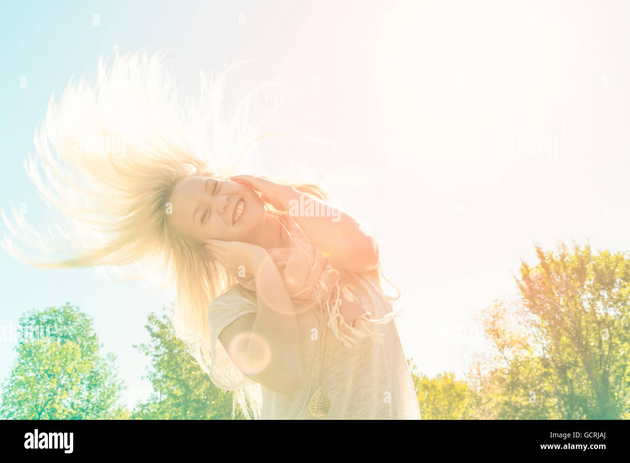 Belle jeune femme l'écoute de la musique et chanter tout en balançant ses longs cheveux blonds en plein air dans un parc de la ville ; Edmonton, Alberta, Canada Banque D'Images