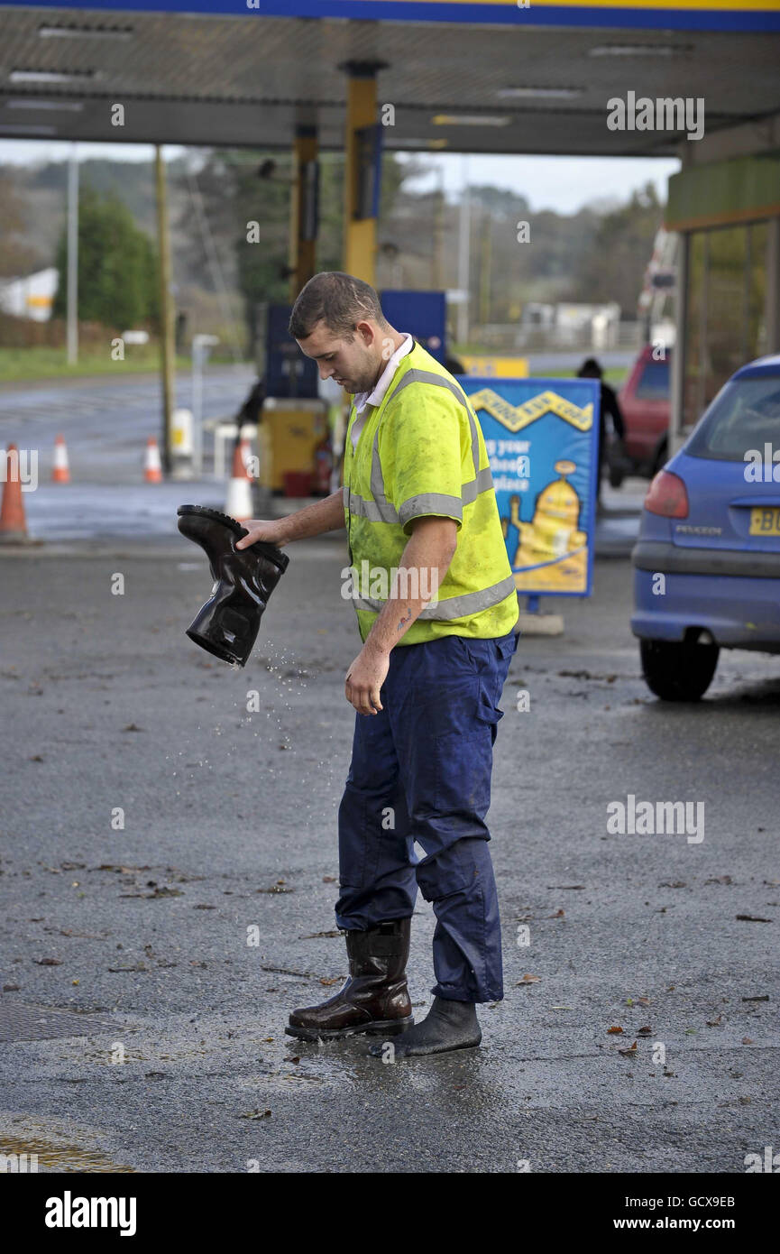 Un ouvrier qui tente de nettoyer les drains vide ses bottes d'eau à St Blazey, en Cornouailles, où les inondations ont fermé le village et causé des ravages. Banque D'Images