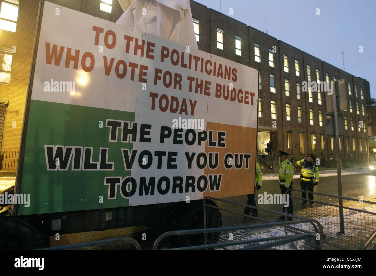 Gardai se trouve à côté d'un préparateur de cerises couvert par un certain nombre de slogans qui s'attaquent aux politiciens et au secteur bancaire pour protester devant les portes de Leinster House, Dublin, le Budget Day. Banque D'Images