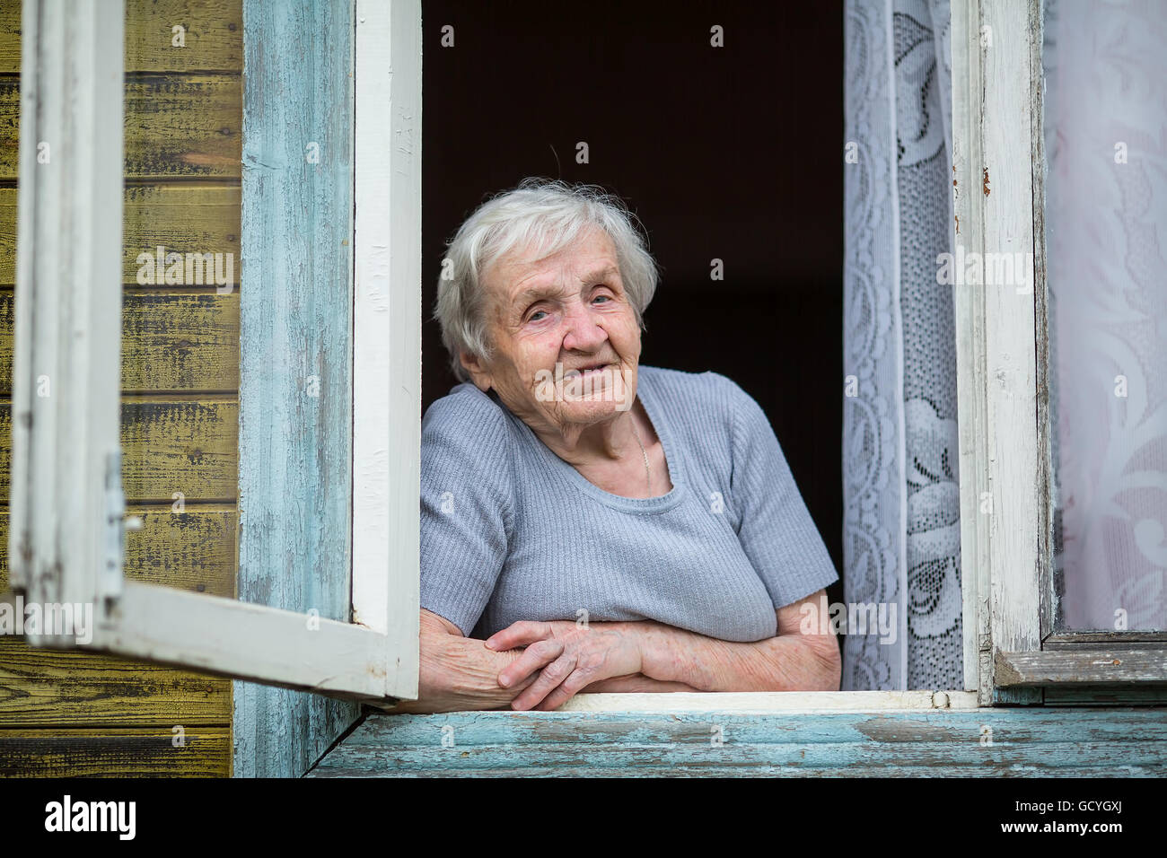 Une femme âgée s'ouvre à partir de la fenêtre de sa chambre. Banque D'Images