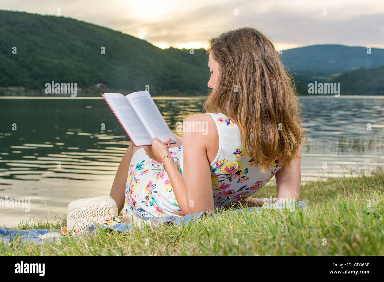 Jeune femme lisant un livre par le lac. Relaxation Solo Banque D'Images