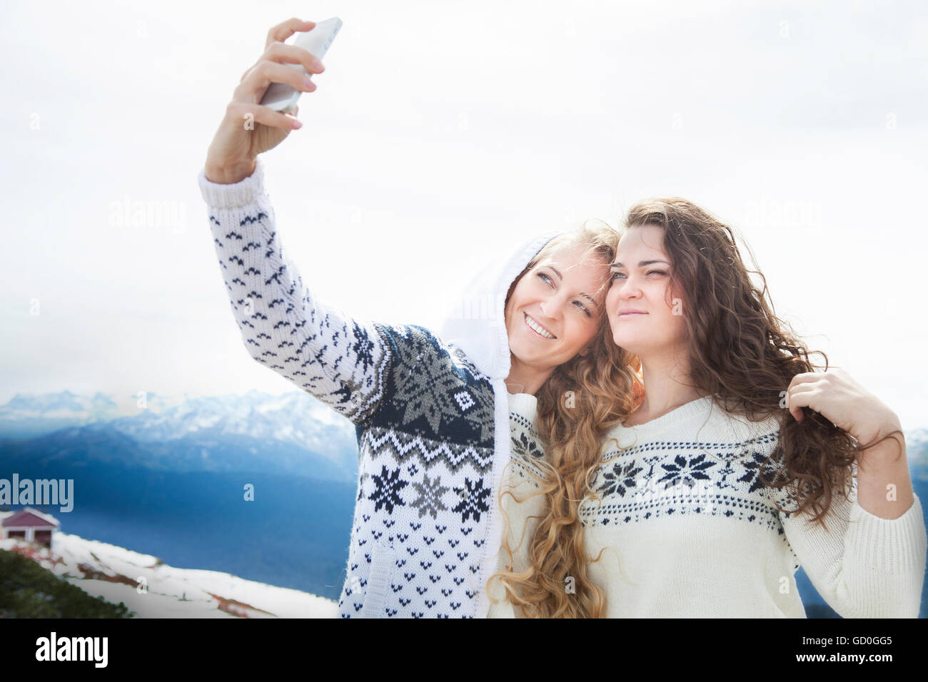 Heureux soeurs photographier une en selfies les vacances d'hiver, avec la montagne enneigée en arrière-plan Banque D'Images