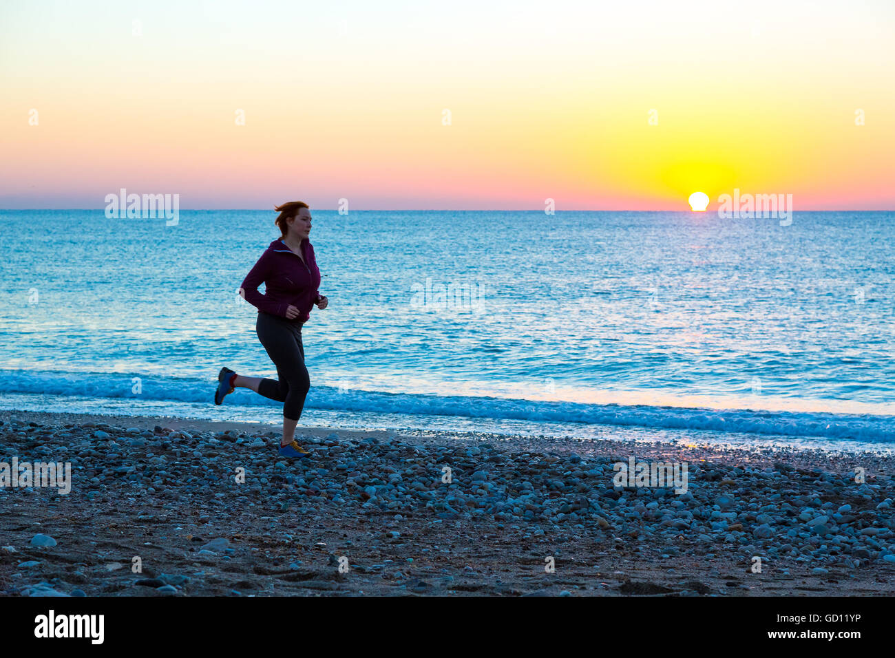 Jeune femme jogging le long de la plage de surf de mer au lever du soleil Banque D'Images