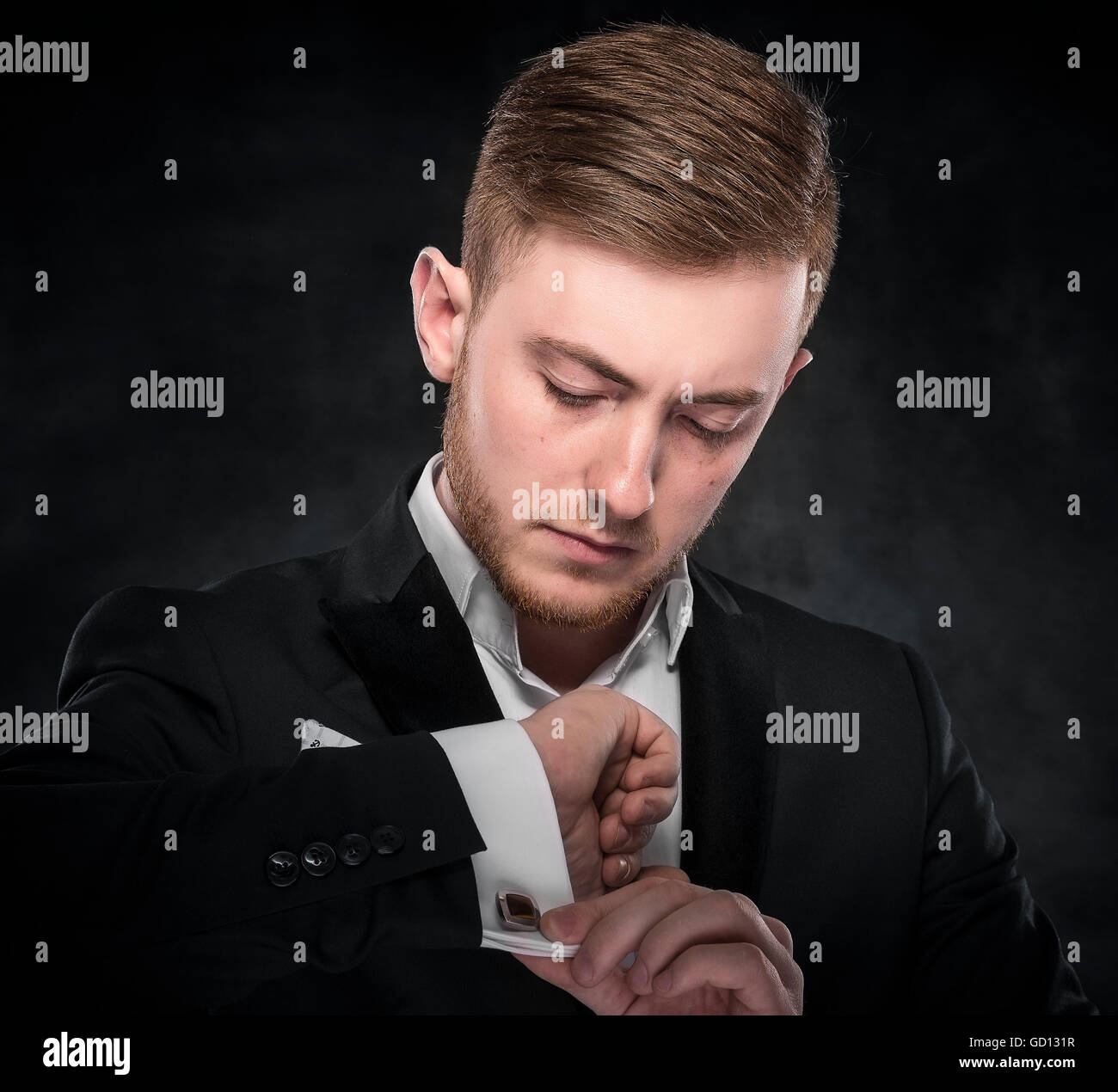 Jeune élégante mode homme regardant sa manchette sur fond sombre. Banque D'Images
