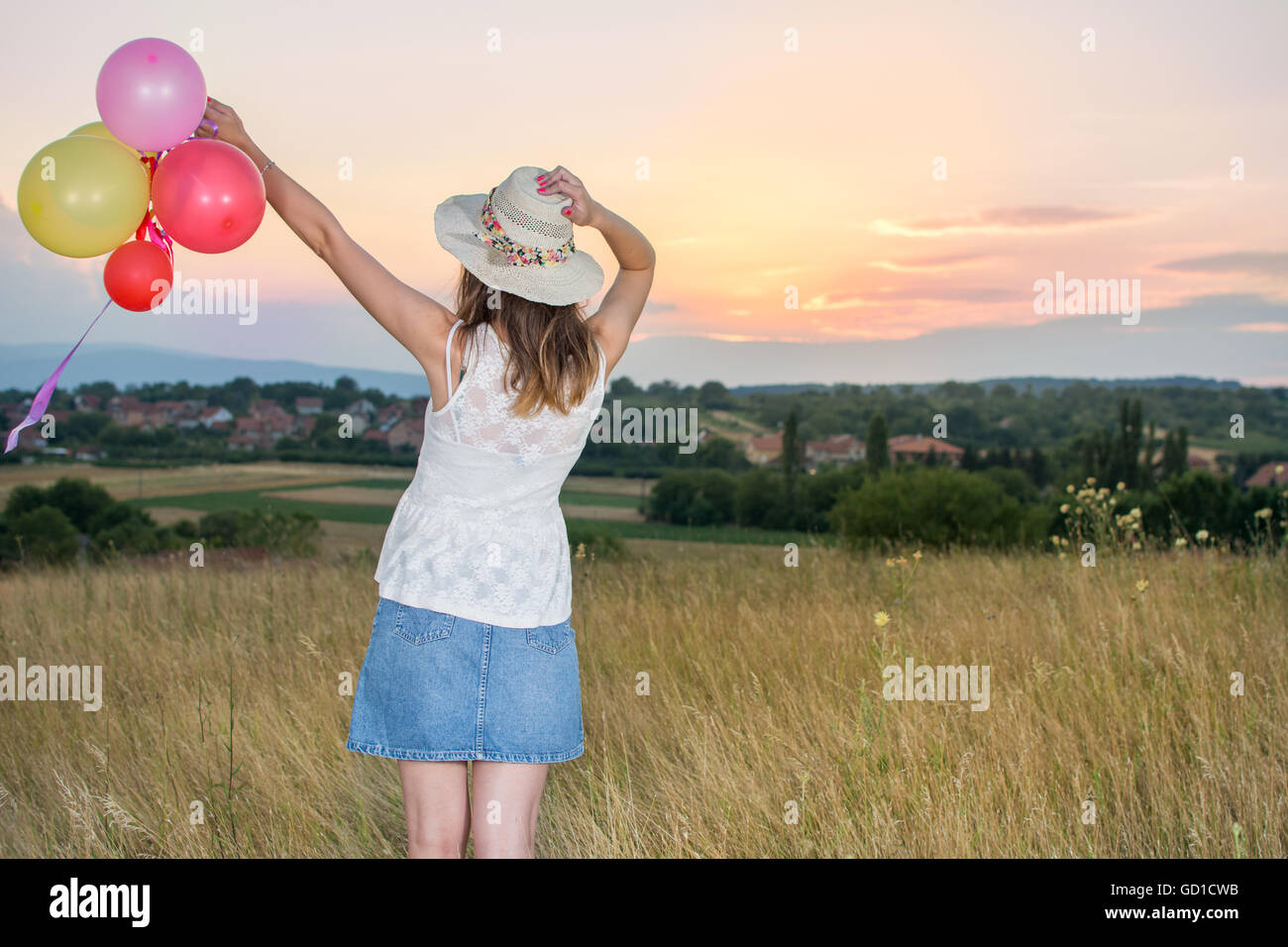 Jeune femme tenant des ballons et à la recherche au coucher du soleil Banque D'Images