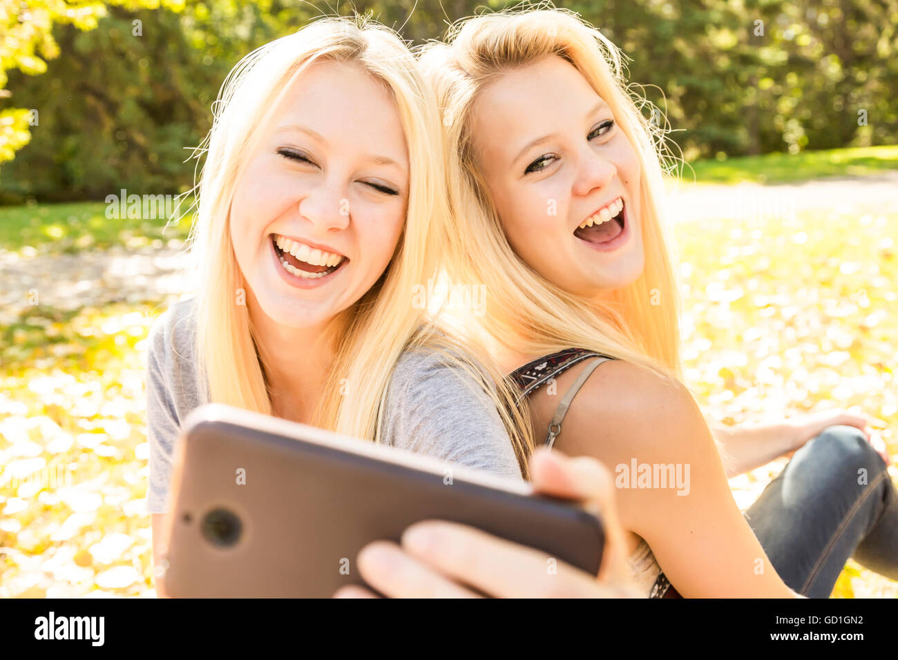 Deux sœurs s'amuser en plein air dans un parc de la ville, à l'automne et rire des autoportraits qu'ils ont prises d'eux-mêmes ; Edmonton, Alberta, Canada Banque D'Images