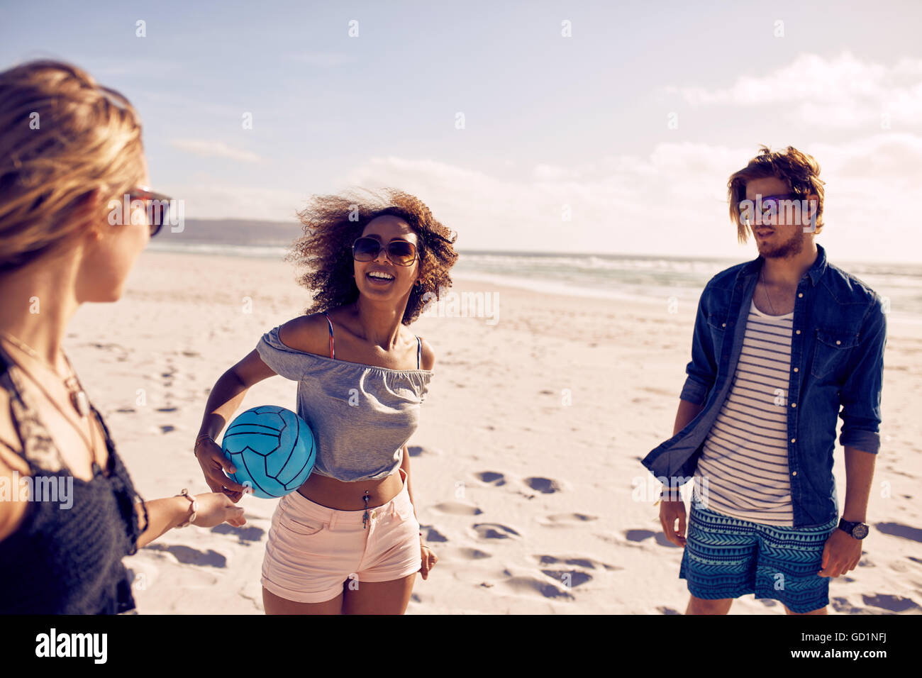 Portrait de jeune femme africaine sur la plage tenant une balle avec les amis en attente. Groupe d'amis au bord de la mer sur une somme Banque D'Images