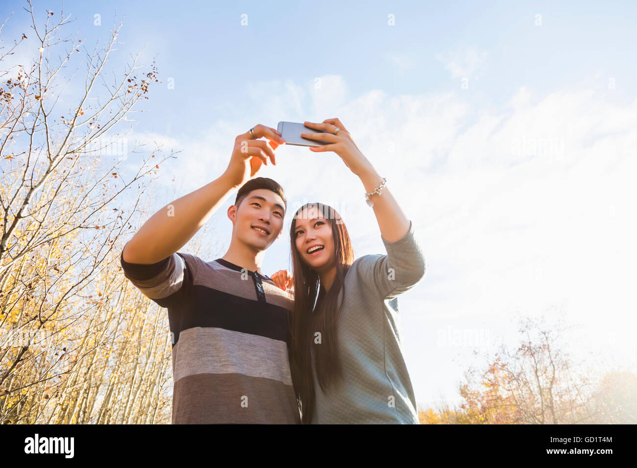 Un jeune couple asiatique appréciant des moments de qualité ensemble en plein air dans Un parc en automne et prenant des autoportraits à l'aide D'Un téléphone intelligent dans la fin de Afternoo... Banque D'Images
