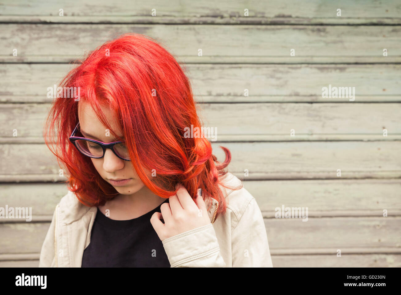 Caucasian teenager girl à lunettes avec des cheveux rouge vif, portrait en extérieur gros plan sur green grungy wooden wall Banque D'Images