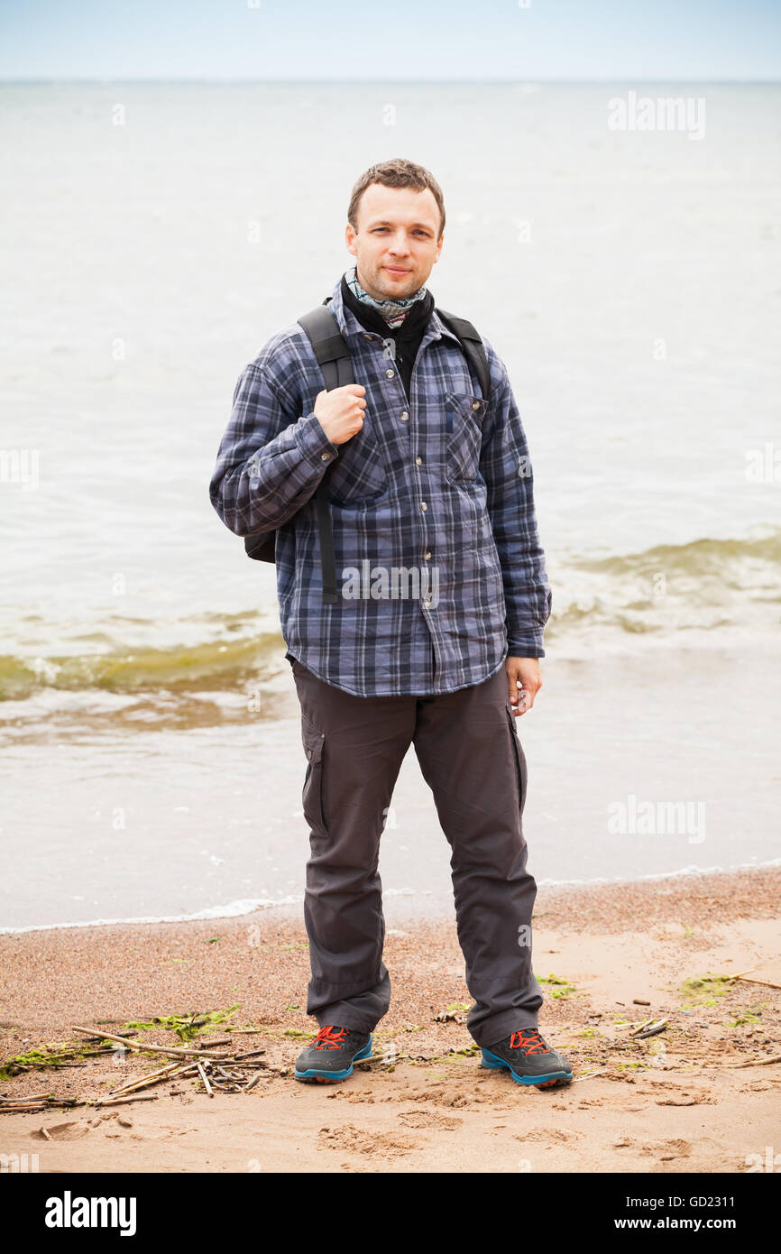 Voyageur en côte de la mer Baltique. Young adult Caucasian man dans des vêtements de plein air avec sac à dos, se dresse sur une plage de sable vide Banque D'Images