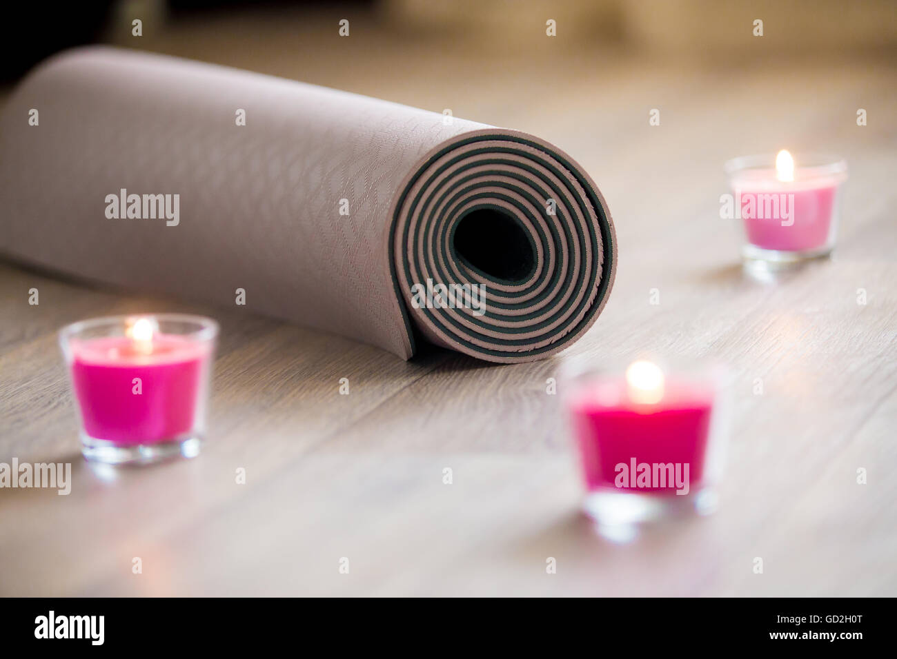 Éclairé de couleur rose bougie de cire rose et marron laminé mat pilates, yoga sur le sol prêt à l'entraînement. Close up. La vie saine Banque D'Images