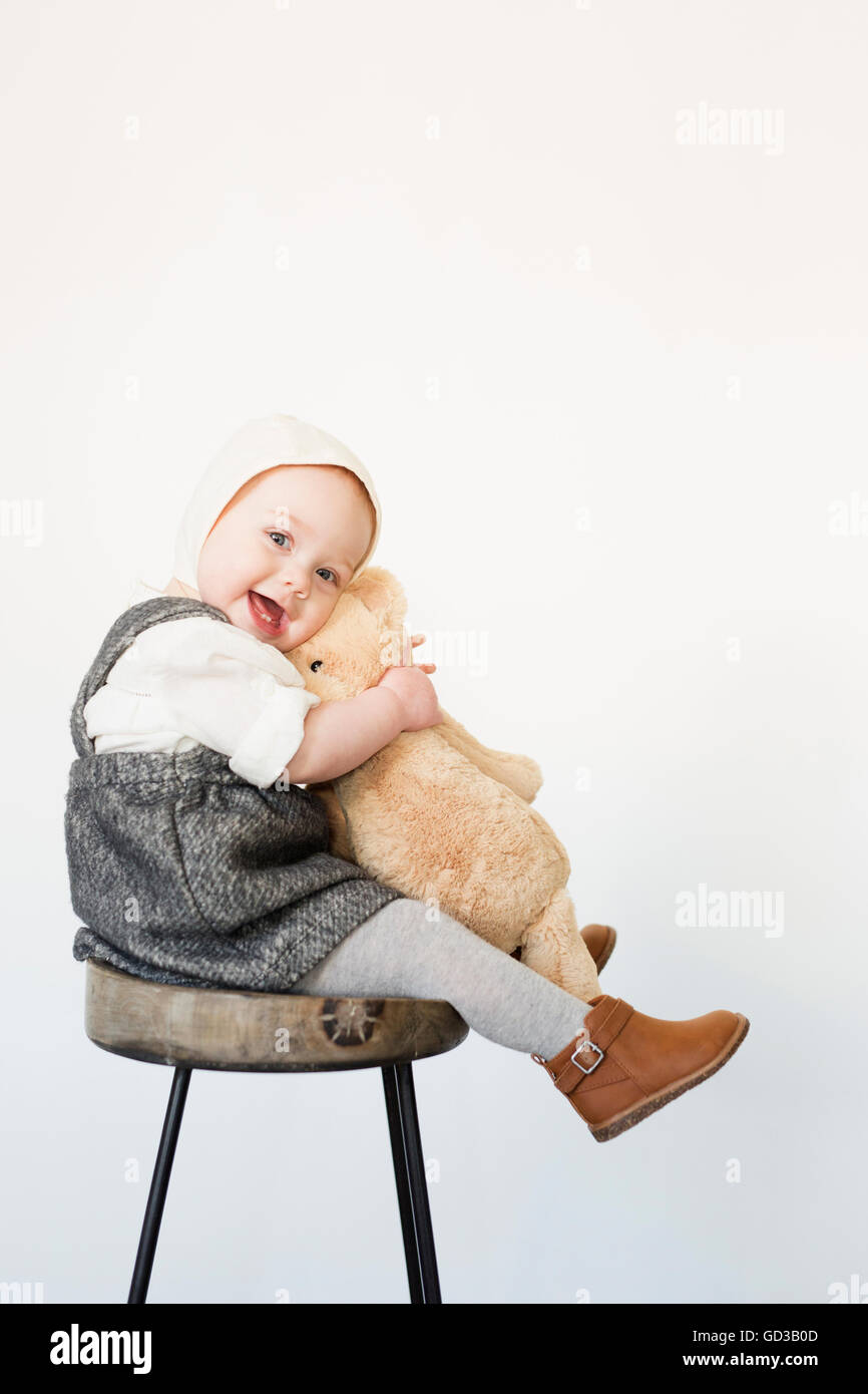 Un jeune enfant, une fille assise sur un grand tabouret holding a teddy bear. Banque D'Images